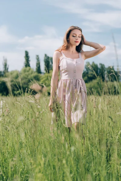 Young pensive woman in stylish dress with long hair walking in meadow alone — Stock Photo