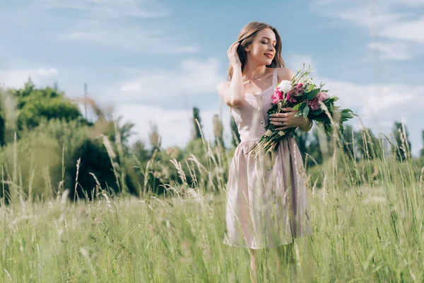 Portrait of beautiful young woman holding bouquet of flowers while standing in field alone — Stock Photo