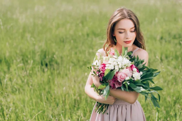 Portrait of beautiful pensive woman holding bouquet of flowers while standing in field alone — Stock Photo