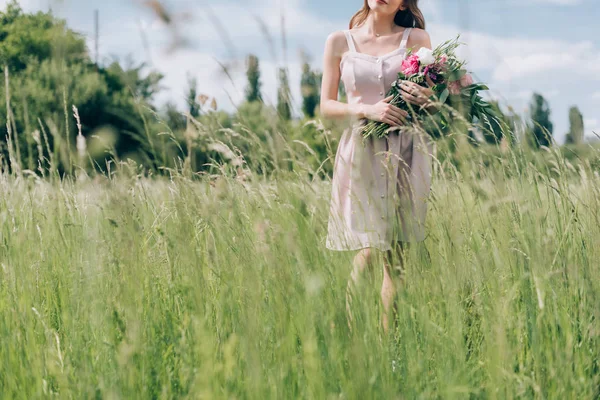 Cropped shot of woman holding bouquet of flowers while standing in field alone — Stock Photo