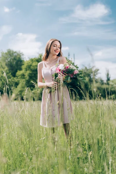 Красива усміхнена жінка тримає букет квітів, стоячи в полі сама — стокове фото