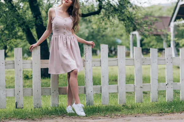 Teilansicht einer lächelnden Frau in stylischem Kleid, die am weißen Zaun auf dem Land steht — Stockfoto
