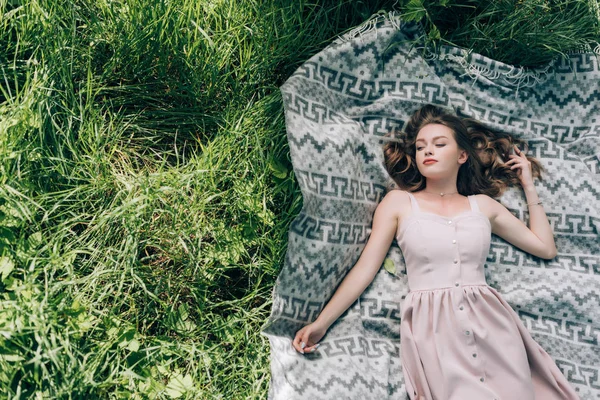 Overhead view of beautiful thoughtful woman in dress lying on blank on green grass in park — Stock Photo