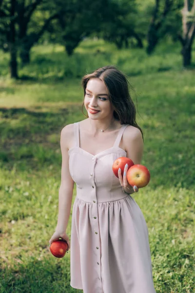 Retrato de sorrindo jovem mulher em vestido com maçãs maduras no campo — Fotografia de Stock