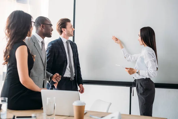 Empresários multiculturais olhando para o conselho branco vazio durante reunião de negócios no escritório — Fotografia de Stock