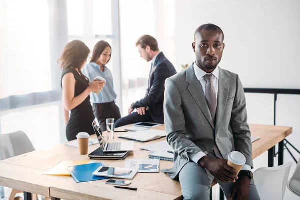 Selektiver Fokus eines afrikanisch-amerikanischen Geschäftsmannes mit Coffee to go und Kollegen am Arbeitsplatz im Büro — Stockfoto
