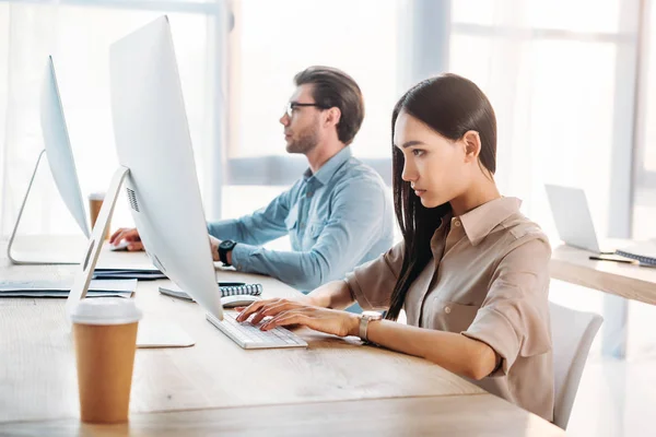 Vista lateral de colegas de negocios interracial enfocados que trabajan en el lugar de trabajo en la oficina - foto de stock