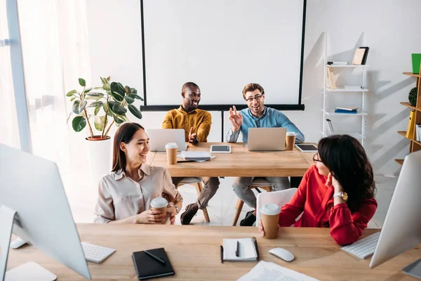 Sorrindo interracial jovens empresários falando durante o trabalho no escritório — Fotografia de Stock