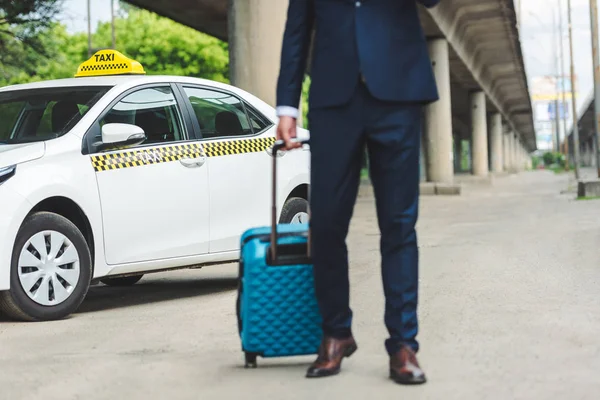 Обрізаний постріл людини в костюмі тримає валізу, стоячи біля таксі — стокове фото