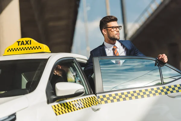 Хенсоме молодий чоловік в костюмі і окулярах дивиться далеко, сидячи в таксі — стокове фото
