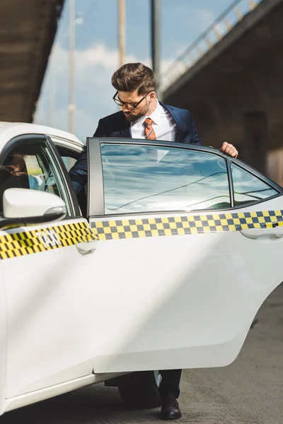 Handsome young man in fashionable suit and eyeglasses opening door of taxi cab — Stock Photo