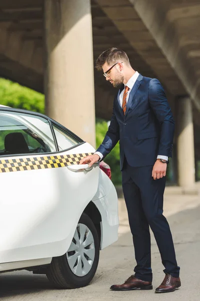 Guapo hombre con estilo en traje abriendo la puerta de taxi taxi - foto de stock