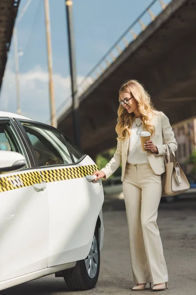 Lächelnde blonde Frau mit Pappbecher öffnet Tür des Taxis — Stockfoto