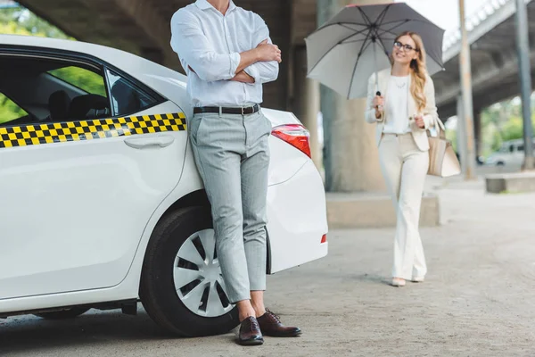 Cropped shot of man leaning at cab while smiling girl with umbrella going to the taxi — Stock Photo