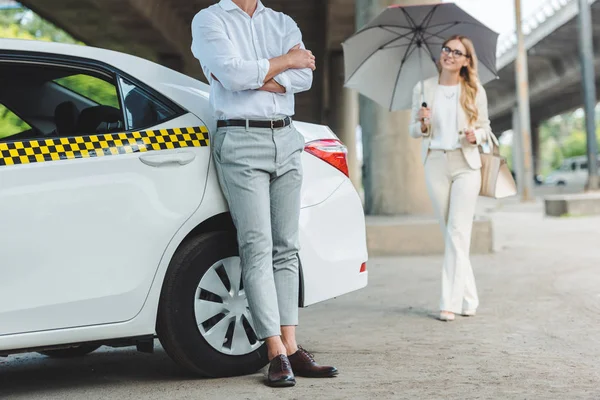 Schnappschuss eines Mannes, der sich an das Taxi lehnt, während lächelndes Mädchen mit Regenschirm zum Taxi geht — Stockfoto