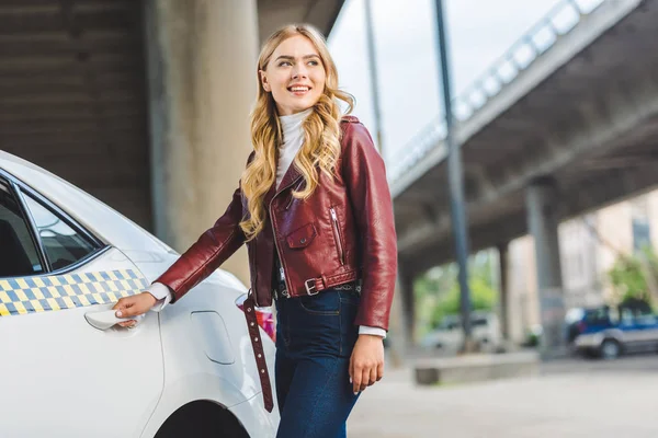 Sorridente giovane donna che apre la porta del taxi e distoglie lo sguardo — Foto stock