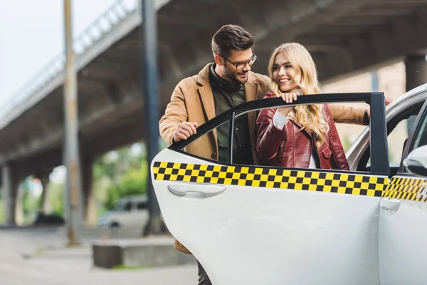 Happy stylish young couple opening door of taxi cab together — Stock Photo