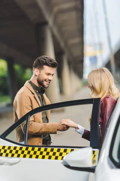 Allegro giovane uomo che tiene la mano sulla bella ragazza mentre in piedi vicino taxi taxi — Foto stock