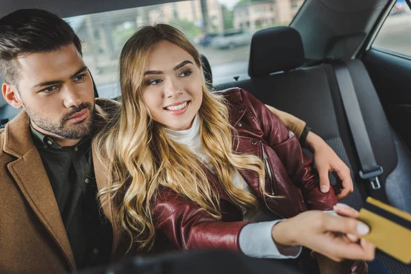 Stylish young couple sitting together in taxi, girl holding credit card — Stock Photo