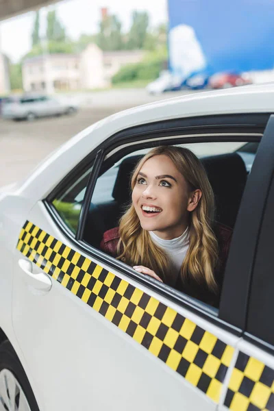 Lächelnde junge Frau blickt durch das Taxifenster nach oben — Stockfoto