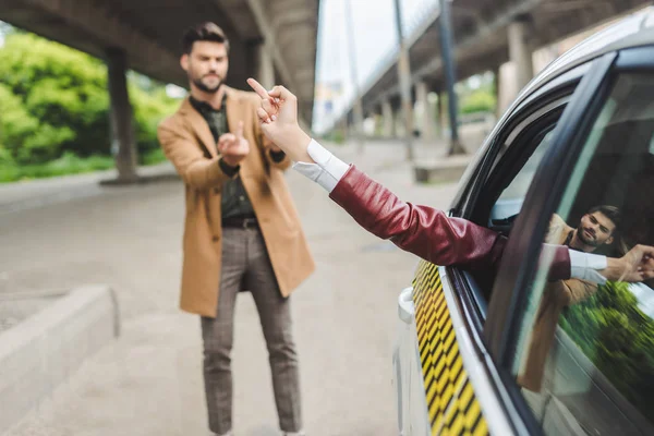 Chica en taxi y hombre en la calle dando los dedos el uno al otro - foto de stock