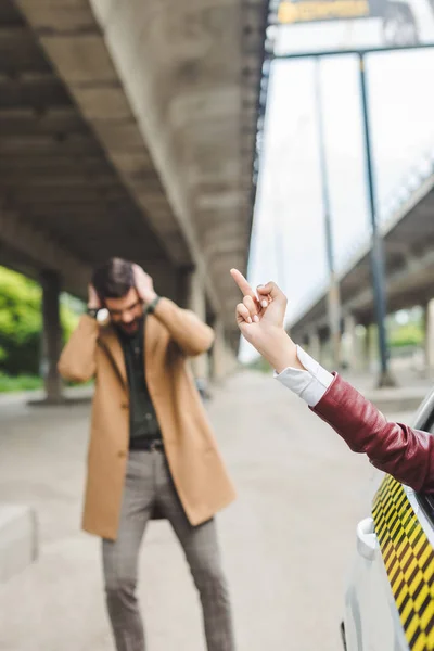 Colpo ritagliato di donna seduta in taxi e dando il dito all'uomo che chiude le orecchie dietro — Foto stock