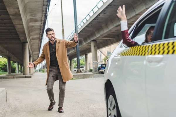 Girl sitting in taxi and waving hand while young man running and looking at car — Stock Photo