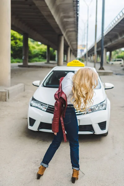 Menina loira vestindo jaqueta de couro e de pé perto de táxi — Fotografia de Stock
