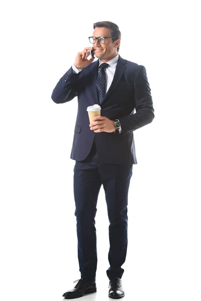 Hombre de negocios sonriente en anteojos hablando en el teléfono inteligente y sosteniendo taza de papel de café aislado sobre fondo blanco - foto de stock