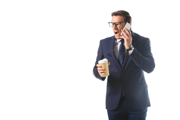 Hombre de negocios enojado en anteojos hablando en el teléfono inteligente y sosteniendo taza de papel de café aislado sobre fondo blanco — Stock Photo