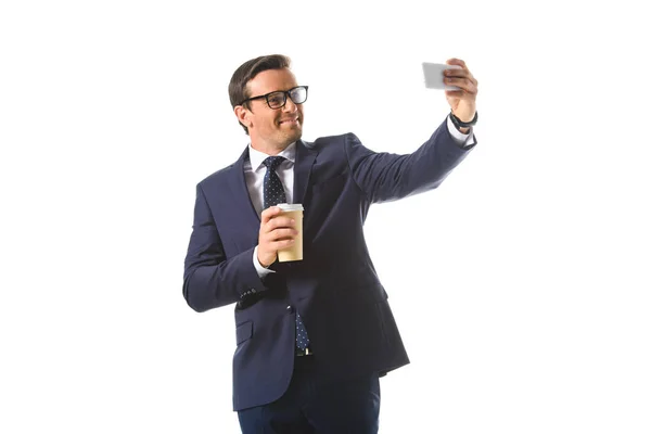 Homme d'affaires souriant dans des lunettes tenant une tasse de café en papier et prenant selfie sur smartphone isolé sur fond blanc — Photo de stock