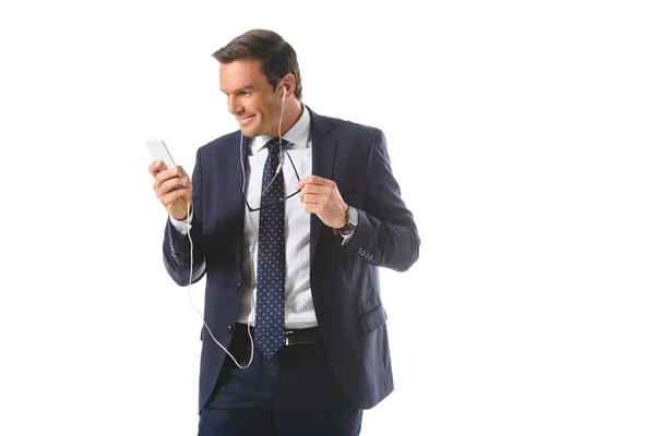 Uomo d'affari sorridente che ascolta musica in auricolare con smartphone isolato su sfondo bianco — Foto stock