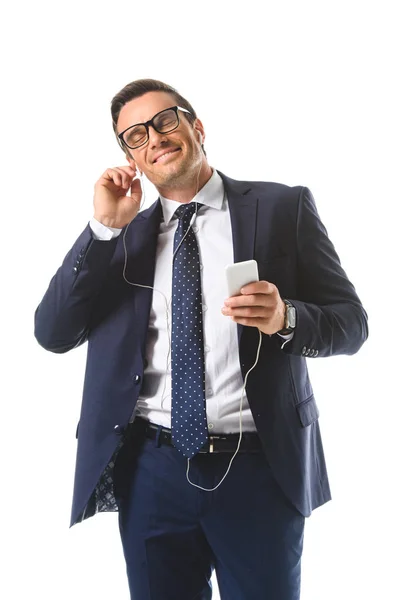 Happy businessman in eyeglasses listening music in earphones with smartphone isolated on white background — Stock Photo