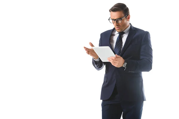 Shocked businessman in eyeglasses gesturing by hand and looking at digital tablet screen isolated on white background — Stock Photo