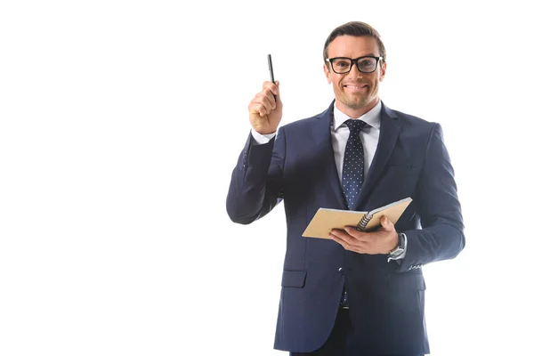 Sonriente hombre de negocios en gafas haciendo gesto de idea por pluma y sosteniendo libro de texto aislado sobre fondo blanco - foto de stock