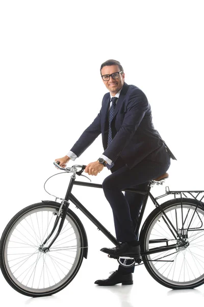 Homme d'affaires souriant avec des lunettes assis sur un vélo isolé sur fond blanc — Photo de stock