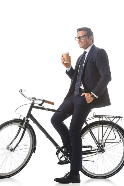 Happy businessman in eyeglasses sitting on bicycle and holding paper cup of coffee isolated on white background — Stock Photo