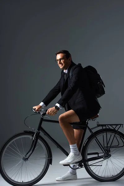 Стильний мужчина з рюкзак, сидячи на велосипеді по сірий фон — стокове фото