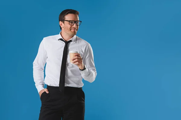 Портрет красивого улыбающегося бизнесмена в очках, держащего бумажную чашку и смотрящего в сторону изолированного на голубом — стоковое фото