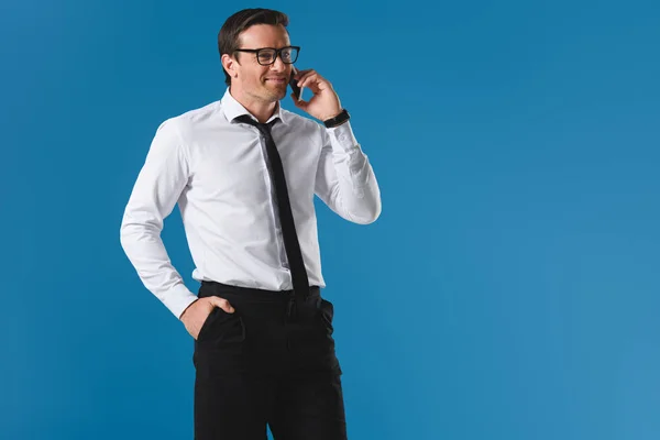 Homme d'affaires souriant dans les lunettes parler par smartphone et regarder loin isolé sur bleu — Photo de stock