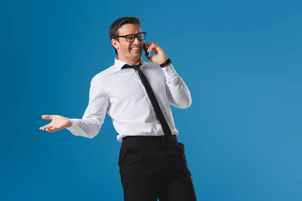 Heureux buisnessman dans les lunettes rire tout en parlant par smartphone isolé sur bleu — Photo de stock