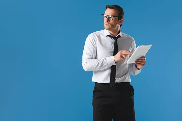 Serious businessman in eyeglasses using digital tablet and looking away isolated on blue — Stock Photo