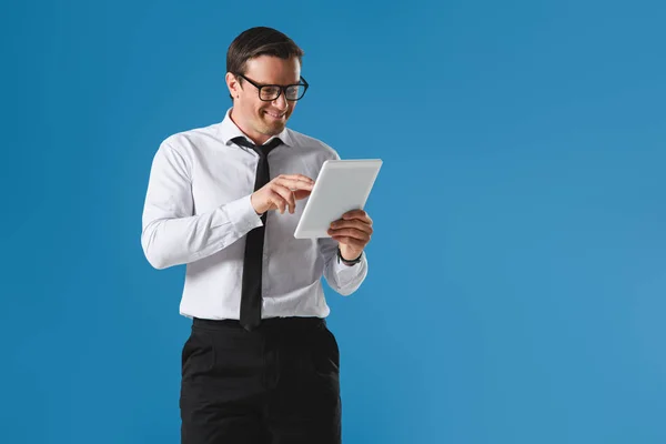 Handsome smiling businessman in eyeglasses using digital tablet isolated on blue — Stock Photo