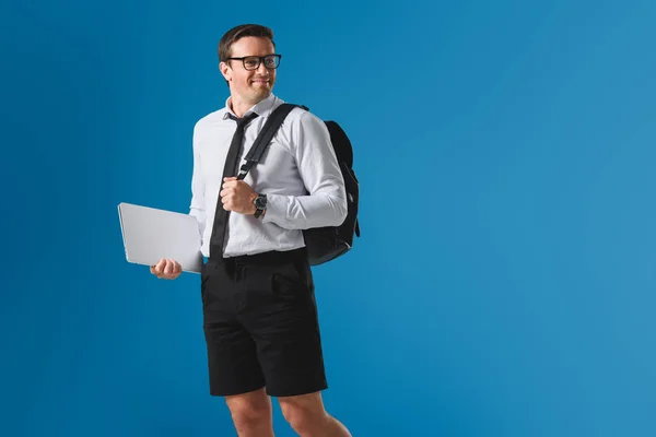 Smiling man with backpack holding laptop and looking away isolated on blue — Stock Photo