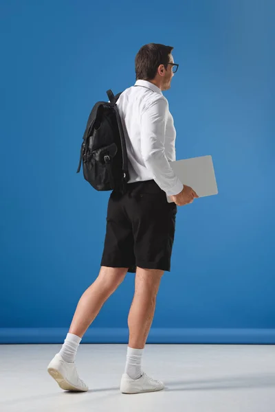 Uomo con zaino che tiene laptop e cammina sul blu — Foto stock