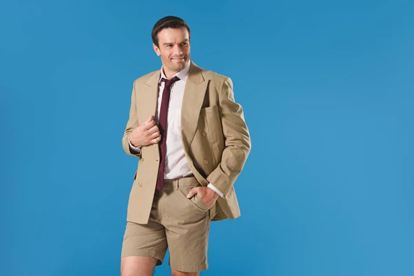 Schöner Mann in Anzugjacke und kurzer Hose, mit der Hand in der Tasche stehend und vereinzelt auf blauem Grund wegschauend — Stockfoto