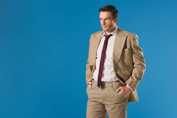 Hombre guapo de pie con las manos en los bolsillos y mirando hacia otro lado aislado en azul - foto de stock