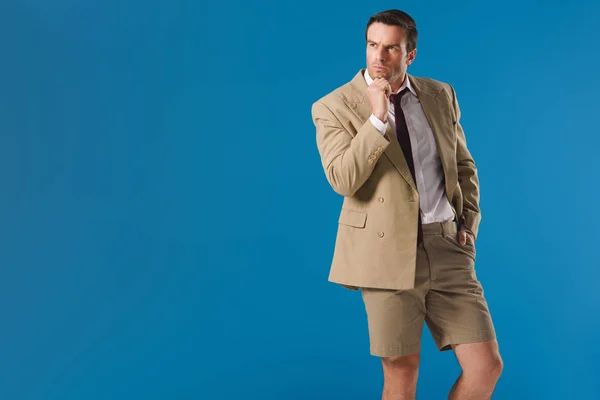 Uomo premuroso in pantaloncini in piedi con mano sul mento e distogliendo lo sguardo isolato sul blu — Foto stock