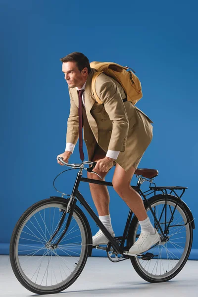 Hombre enfocado con mochila a caballo bicicleta y mirando hacia otro lado en azul - foto de stock