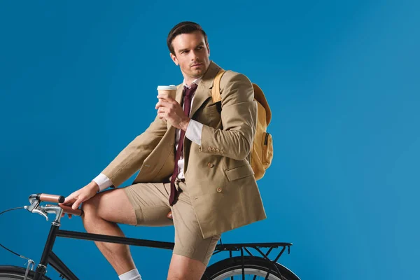 Homme tenant tasse en papier tout en vélo et regardant loin isolé sur bleu — Photo de stock